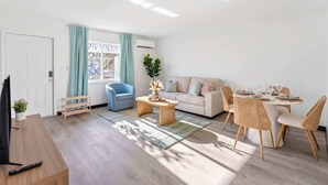Un salon moderne avec un canapé, une table à manger, des chaises, un téléviseur et une fenêtre avec des rideaux.