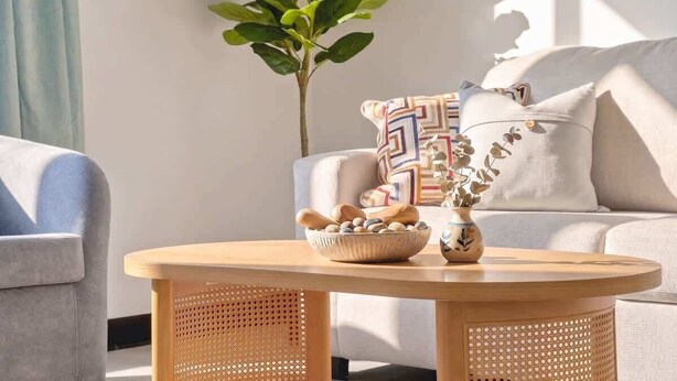 Un salon avec une table ronde en bois, un canapé, une plante en pot et un vase décoratif.