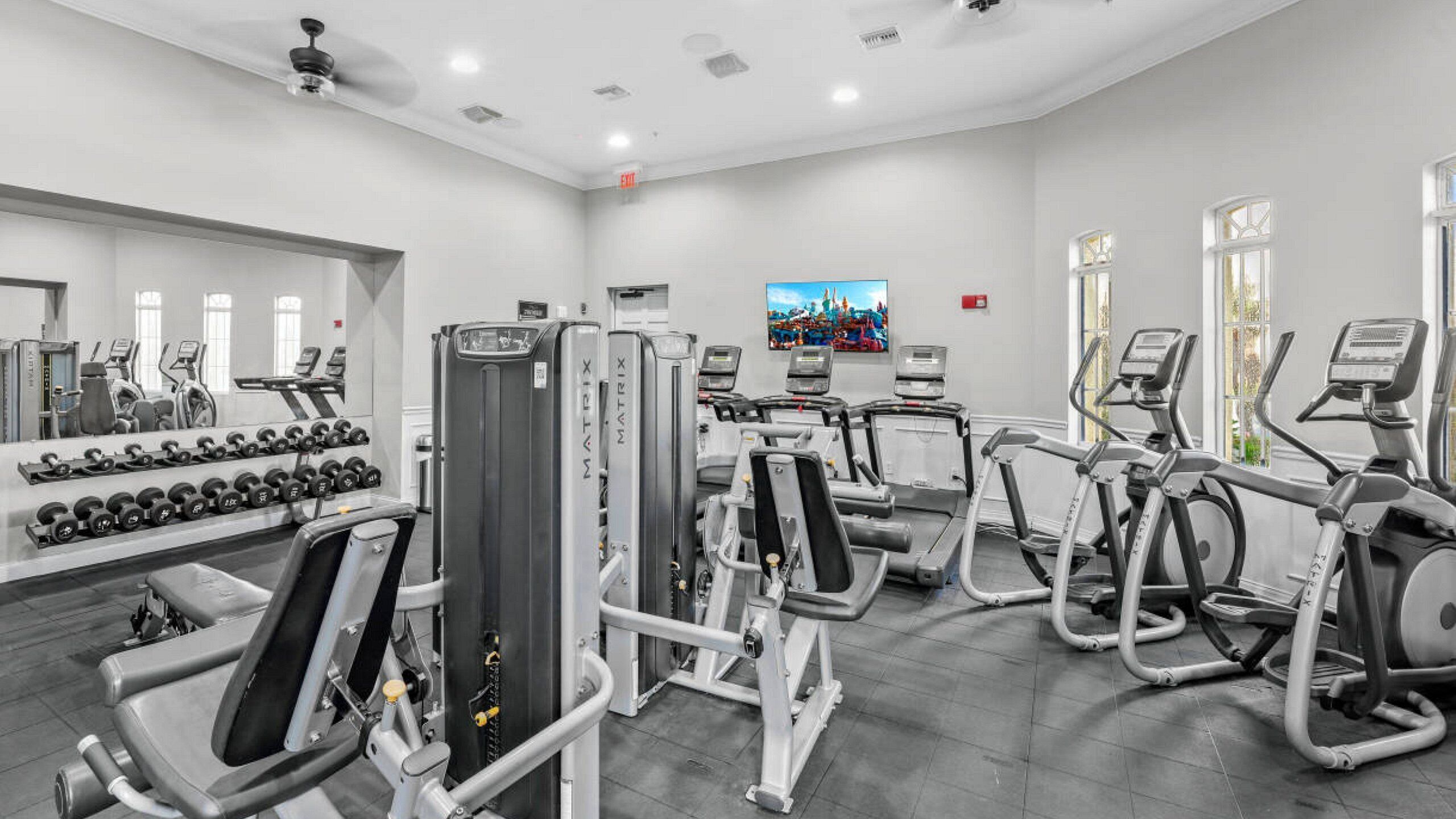 A gym with various exercise machines, dumbbells, and a large mirror.