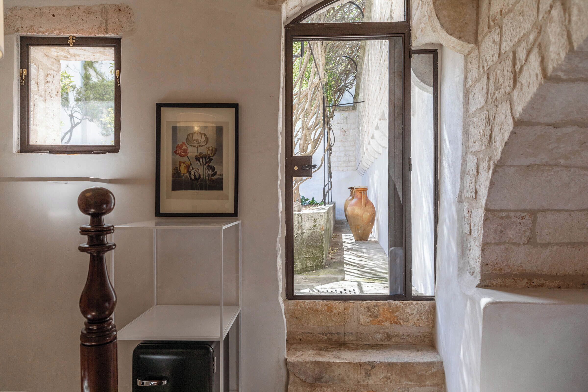A staircase with stone walls, a wooden balustrade, a framed picture, and a large vase in the background.