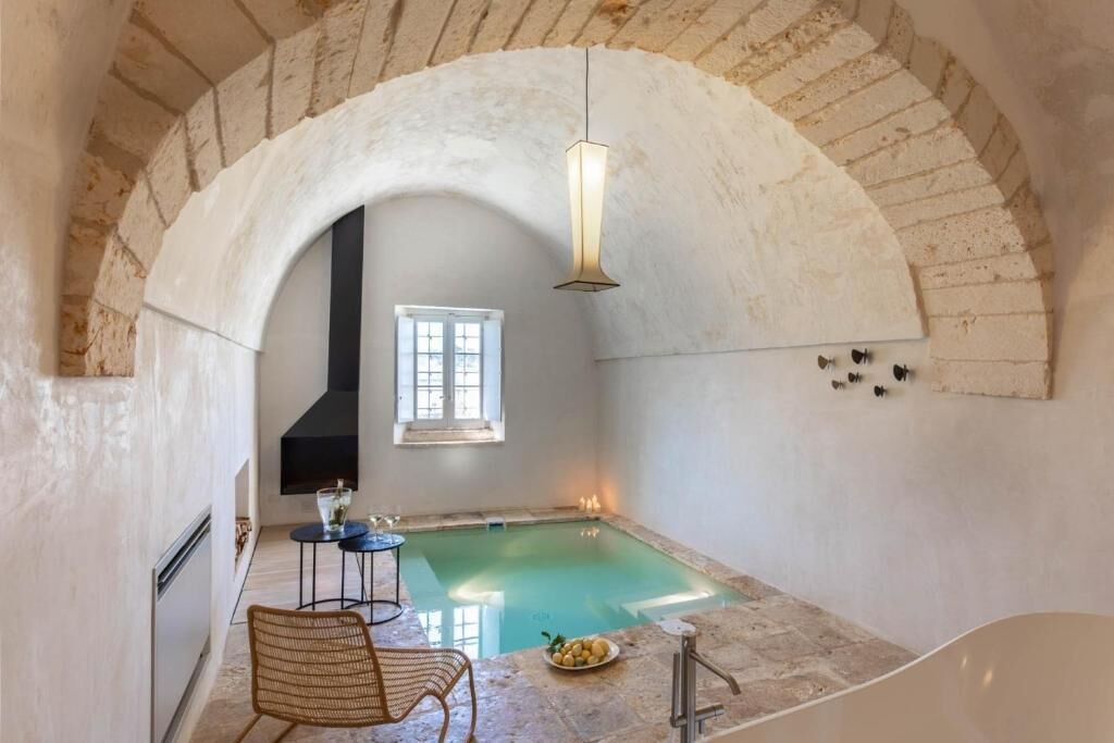 Un'area benessere con piscina, una poltrona, un tavolo e una bottiglia di vino.