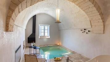 Un'area benessere con piscina, una poltrona, un tavolo e una bottiglia di vino.