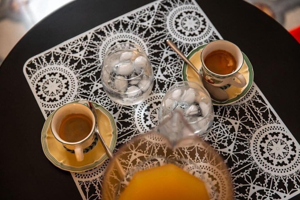 Taula amb un llençol estampat, dues tasses de te, un got amb cubs de gel i un got de suc d'aranja.