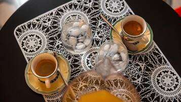 Una mesa con mantel estampado, dos tazas de té, un vaso con cubitos de hielo y un vaso de jugo de naranja.