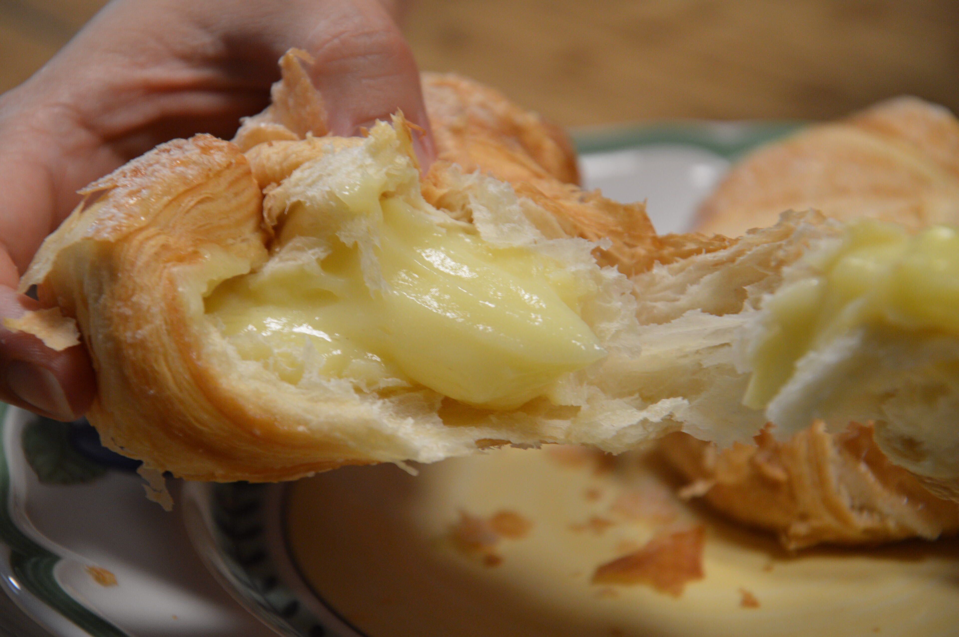 A hand holding a pastry with a creamy filling, on a plate with a floral pattern.
