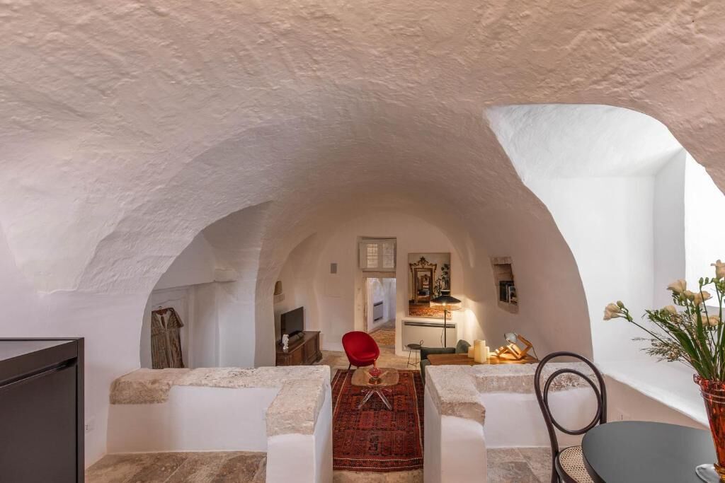 A cozy, arched room with a stone bench, a red chair, and a small table with a rug.