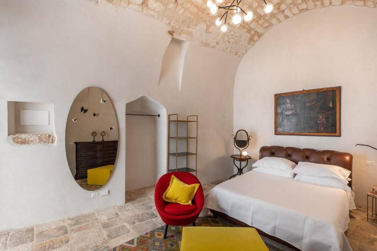 A bedroom with a bed, a red chair, a mirror, and a painting on the wall.