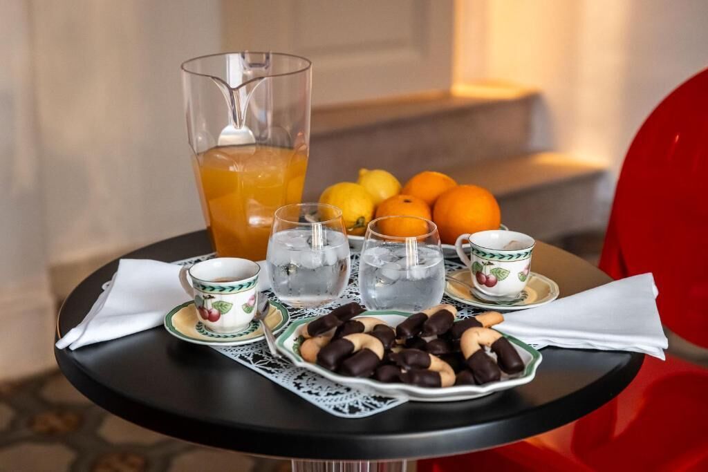 A table with a pitcher of orange juice, glasses of water, oranges, and a plate of nuts and chocolates.