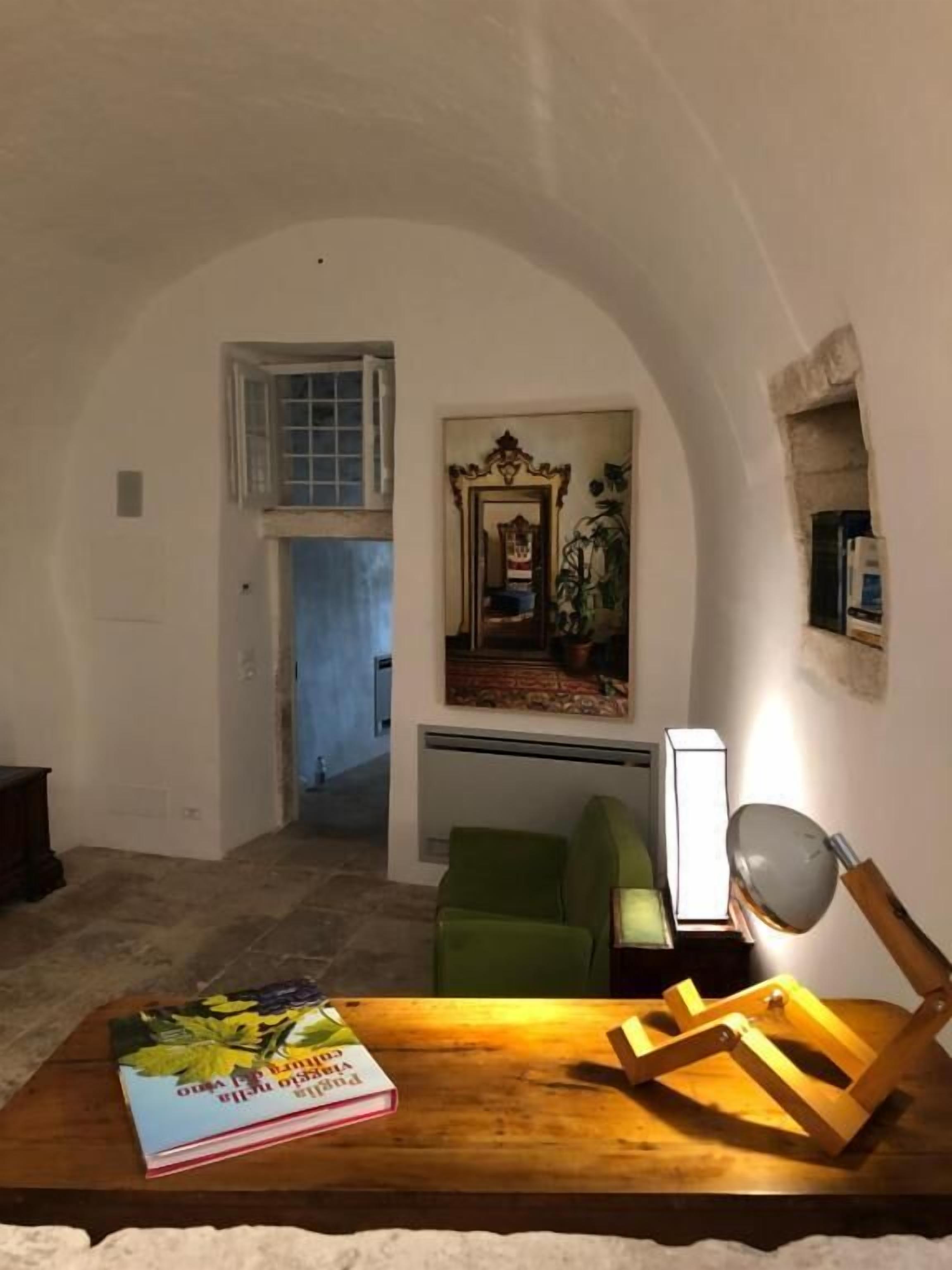 A room with a wooden table, a green chair, a framed picture, and a mirror.