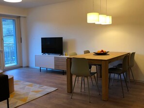 A modern dining area with a wooden table, chairs, a television, and a fruit bowl. - Perle "Balmhoru" # 5-bed apartment, Dusche, WC 5-Bettwohnung, Dusche, WC by Interhome (Leukerbad)