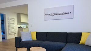 Ett modernt vardagsrum med en grå hörnsoffa, två träbord och en matta med geometriskt mönster.