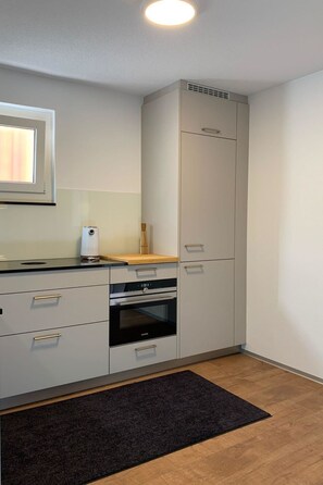 Una cucina compatta con forno a incasso, microonde e piano di lavoro in legno.