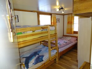 A bunk bed room with wooden frames, a lower bunk with a dolphin-themed bedspread, and a single bed with a floral bedspread. - Chalet Kondore 1 # 5-bed apartment, Dusche, WC 5-Bettwohnung, Dusche, WC by Interhome (Leukerbad)