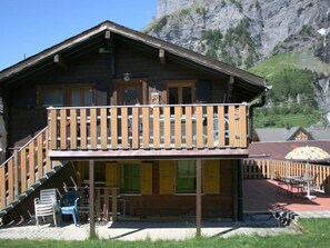 A wooden chalet with a balcony, outdoor seating, and a mountain backdrop. - Chalet Kondore 1 # 5-bed apartment, Dusche, WC 5-Bettwohnung, Dusche, WC by Interhome (Leukerbad)