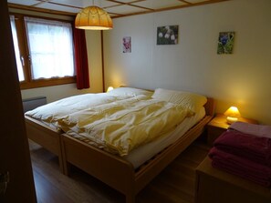 A single-bed room with a wooden frame, a window with curtains, a bedside lamp, and a wall-mounted artwork. - Chalet Kondore 1 # 5-bed apartment, Dusche, WC 5-Bettwohnung, Dusche, WC by Interhome (Leukerbad)