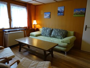 Una habitación acogedora con piso de madera, un sofá verde con cojines estampados, una mesita, un teclado y una lámpara.