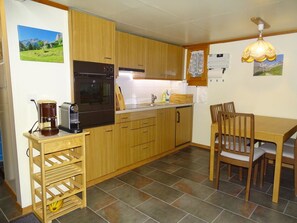 A kitchen with wooden cabinets, a built-in oven, a coffee maker, and a dining table with chairs. - Chalet Kondore 1 # 5-bed apartment, Dusche, WC 5-Bettwohnung, Dusche, WC by Interhome (Leukerbad)