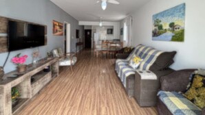 A living room with a TV, wooden flooring, a ceiling fan, and a sofa. - Vacation rental apartment in the center of Canasvieiras. (Florianópolis)