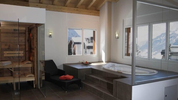 A modern bathroom with a bathtub, a glass shower enclosure, and a view of mountains through large windows. - Residenz Iris Leukerbad # 4-bed apartment, Dusche und Bad, WC by Interhome (Leukerbad)