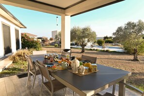 An outdoor dining area with a table set for breakfast, surrounded by chairs, with a view of a residential neighborhood and trees. - Room "Chambre 3" with Mountain View, Shared Pool and Wi-Fi (Aléria)