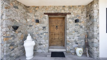 A stone wall entrance with a wooden door, a white urn, and a decorative pot.
