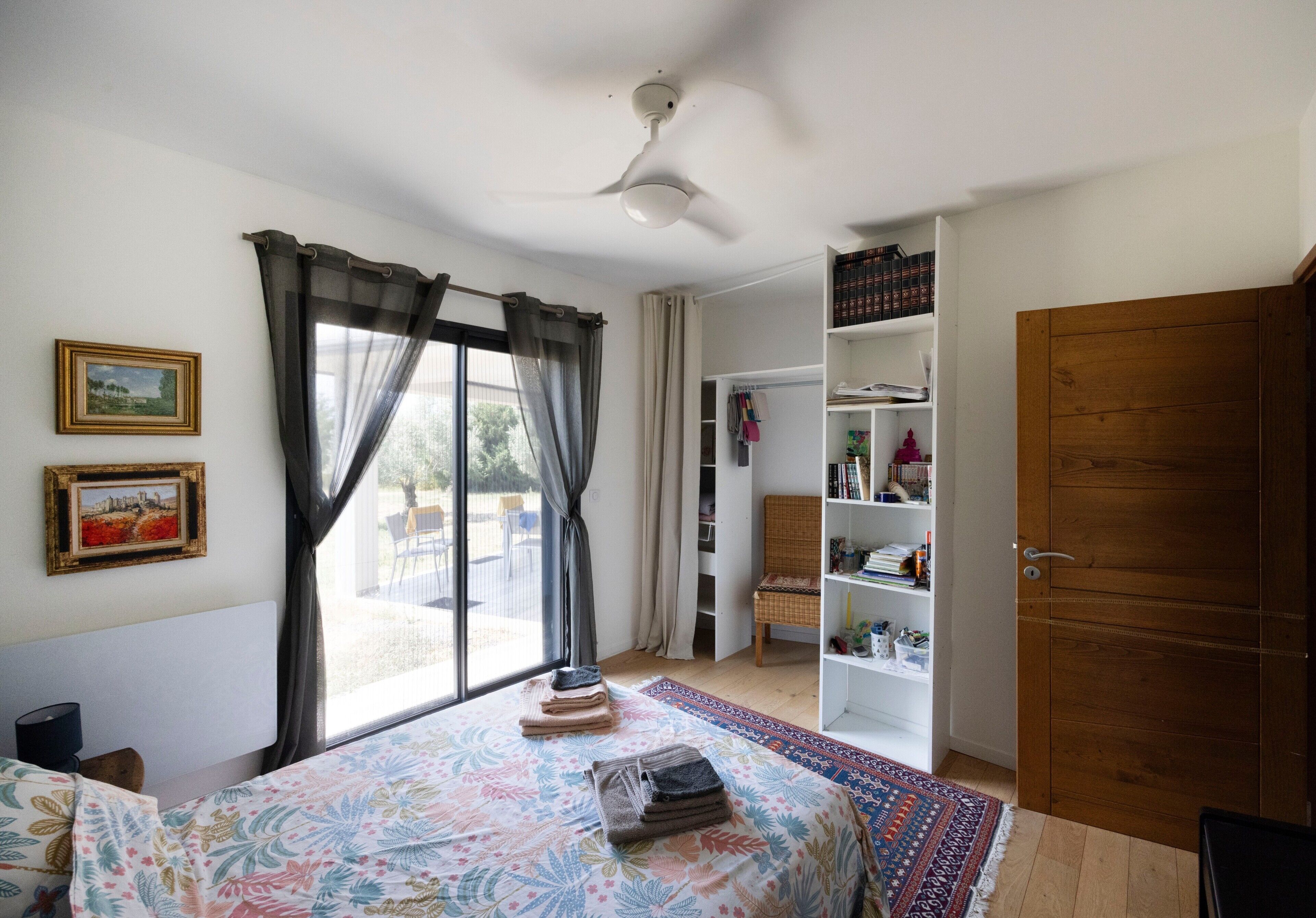 Ein Schlafzimmer mit Bett, einem Fenster mit Vorhängen, einem Bücherregal und einem Kleiderschrank.