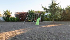A playground with a swing set and a slide in a grassy area with trees and a building in the background.