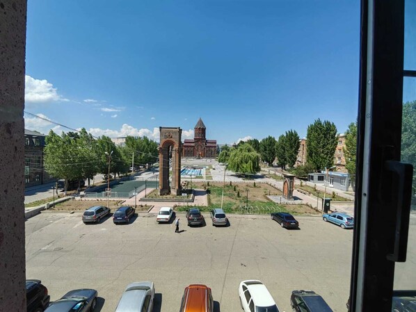 A parking lot with several cars, a central monument, and a building with a dome in the background.