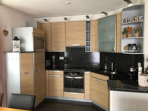 A modern kitchen with wooden cabinets, a built-in oven, a microwave, and a coffee machine. - Edelweiss A 11 # 4-bed apartment, Dusche, WC 4-Bettwohnung, Dusche, WC by Interhome (Leukerbad)