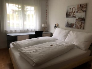 Un dormitorio con cama, escritorio y ventana.