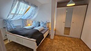 Ein Schlafzimmer mit einem Bett, Nachttischen, einem Kleiderschrank und einem Fenster mit Vorhängen.