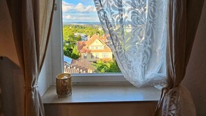 Ein Fenster mit Blick auf eine Stadt, ein Korbwägelchen auf der Fensterbank und Vorhänge.