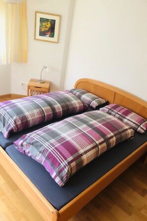 A double bed with a plaid bedspread and pillows, a bedside table with a lamp, and a painting on the wall. - Edelweiss A 31 # 4-bed apartment, Dusche und Bad, WC by Interhome (Leukerbad)