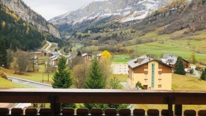 Eine gebirgige Landschaft mit einer sich durch ein Tal schlängelnden Straße, Häusern und einem Gebäude mit einem markanten, hohen Fenster.