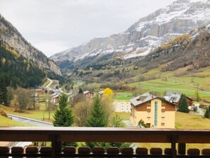 Eine gebirgige Landschaft mit einer sich durch ein Tal schlängelnden Straße, Häusern und einem Gebäude mit einem markanten, hohen Fenster.
