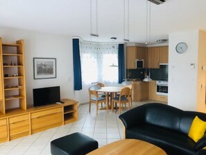 A modern living room with a black sofa, wooden entertainment unit, and a dining area with a table and chairs. - Edelweiss A 31 # 4-bed apartment, Dusche und Bad, WC by Interhome (Leukerbad)