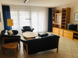 A living room with a sofa, armchair, coffee table, and a TV on a wooden cabinet. - Edelweiss A 31 # 4-bed apartment, Dusche und Bad, WC by Interhome (Leukerbad)