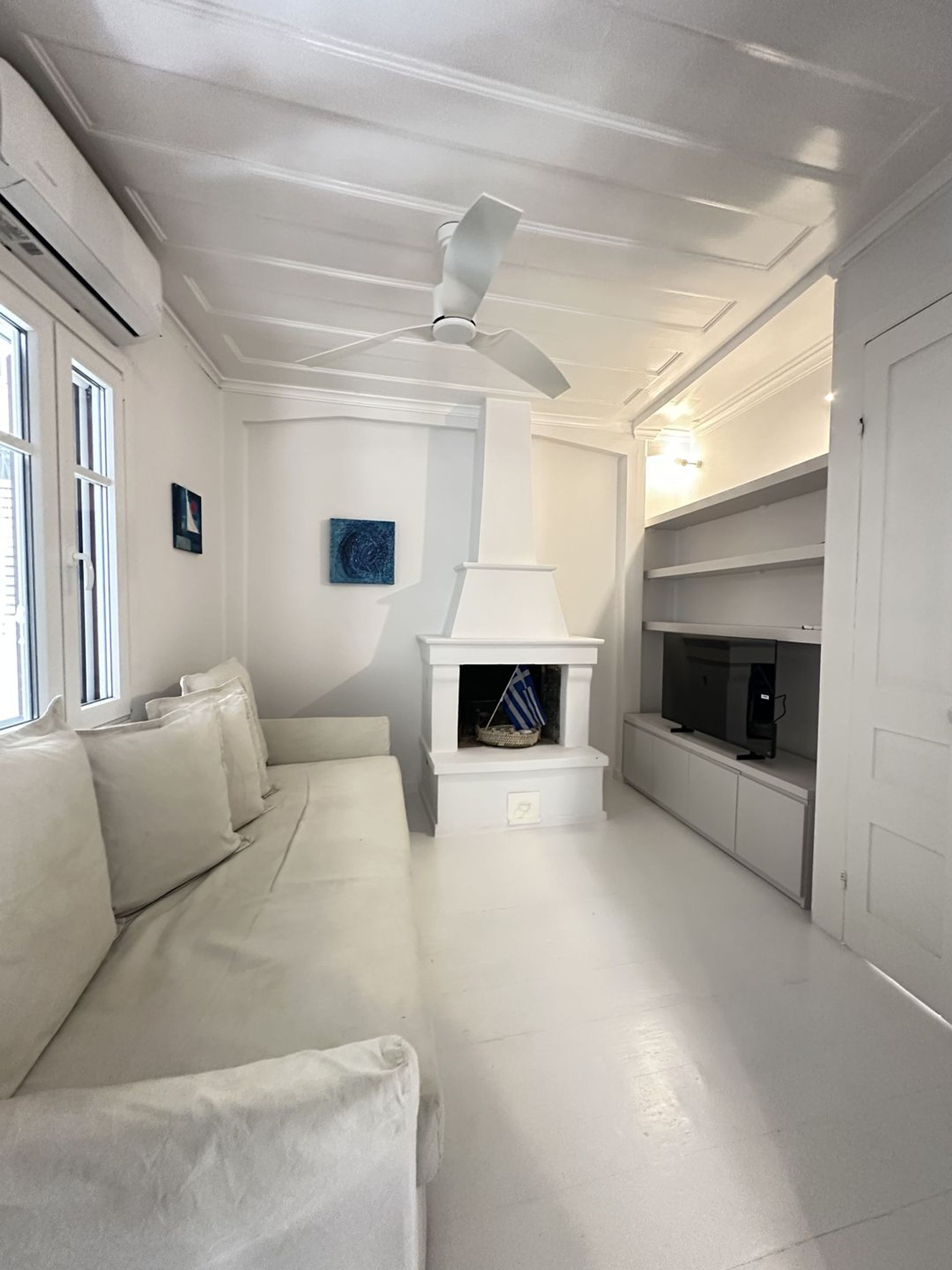 A modern living room with a white sofa, a fireplace, a ceiling fan, and a TV on a shelf.