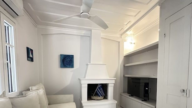 A white room with a sofa, a fireplace, a ceiling fan, and a TV stand. - Sapfous 10 (Lefkada)