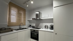 A modern kitchen with white cabinets, a stainless steel sink, a built-in oven, and a coffee maker. - Sapfous 10 (Lefkada)
