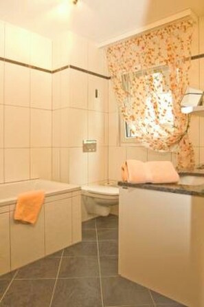 A bathroom with a bathtub, toilet, and sink. - Ambassador B01 # 4-bed apartment, Dusche und Bad, WC by Interhome (Leukerbad)