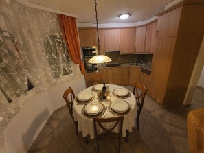 Uma área de refeições com uma mesa redonda posta para quatro pessoas, cercada por cadeiras de madeira.