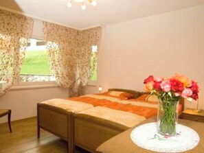 A bedroom with a bed, a bedside table with a vase of flowers, and a window with curtains. - Ambassador B01 # 4-bed apartment, Dusche und Bad, WC by Interhome (Leukerbad)