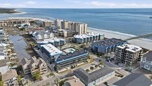 A coastal hotel area with multiple buildings, including a large hotel with a blue roof and a swimming pool, adjacent to a beach and ocean.
