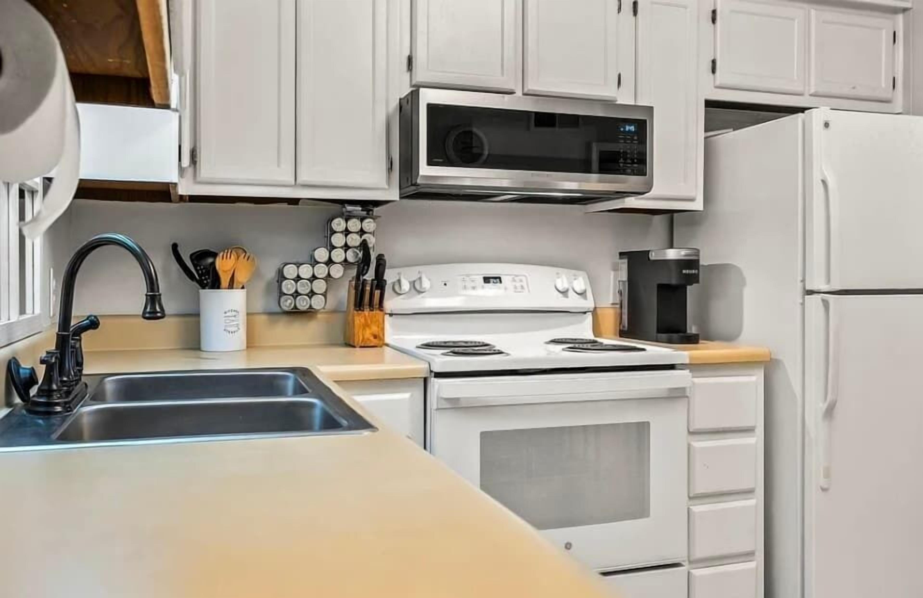 A kitchen with white cabinets, a stove, a microwave, and a refrigerator.
