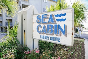 Ein Holzschild für 'Sea Cabin Cherry Grove' mit Wellenmuster.