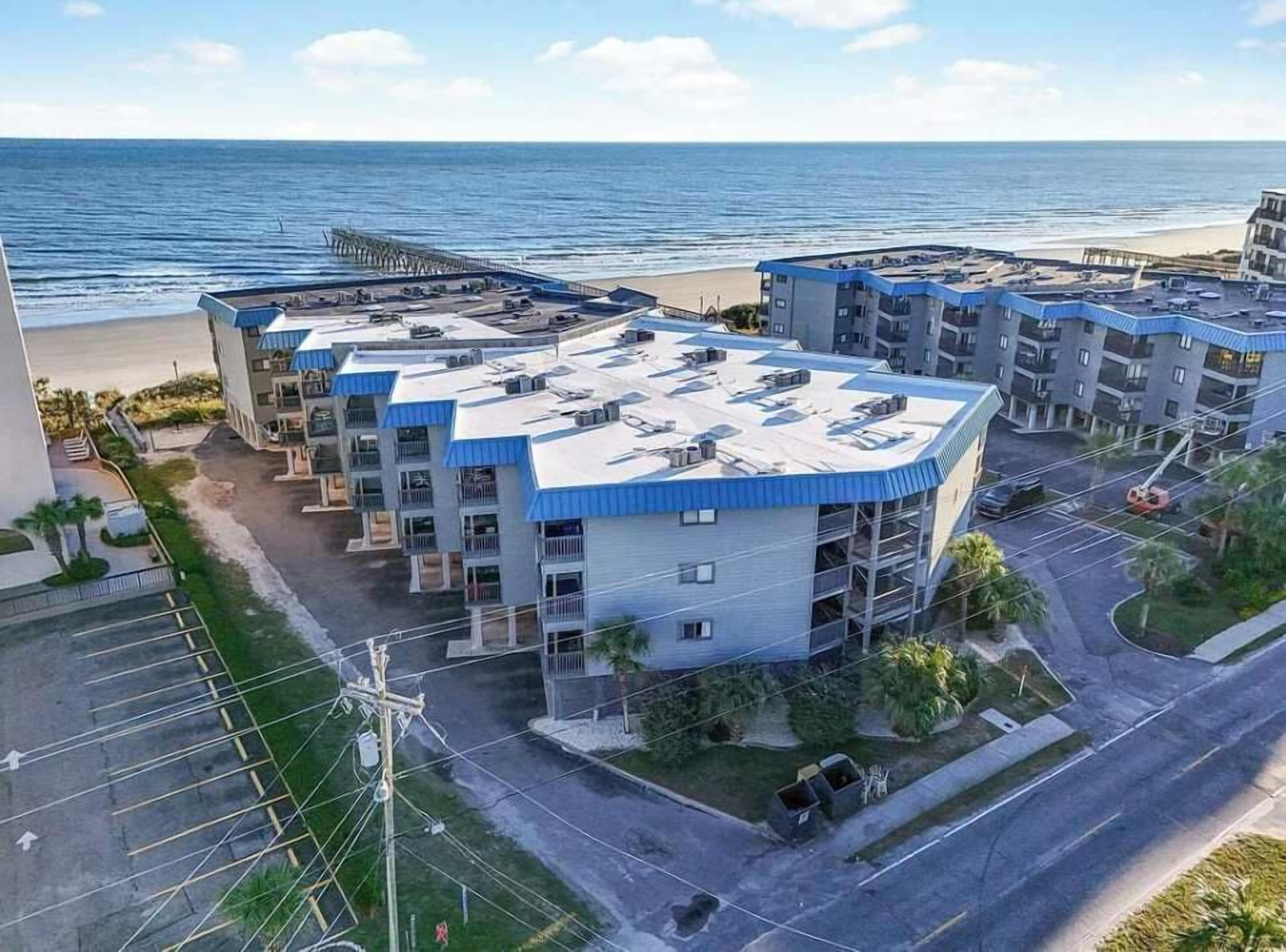 Un hôtel à plusieurs étages doté d’une terrasse sur le toit, situé près d’une plage.