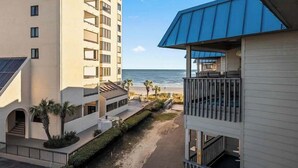 A multi-story hotel with balconies overlooking a beach, a clear sky, and palm trees.