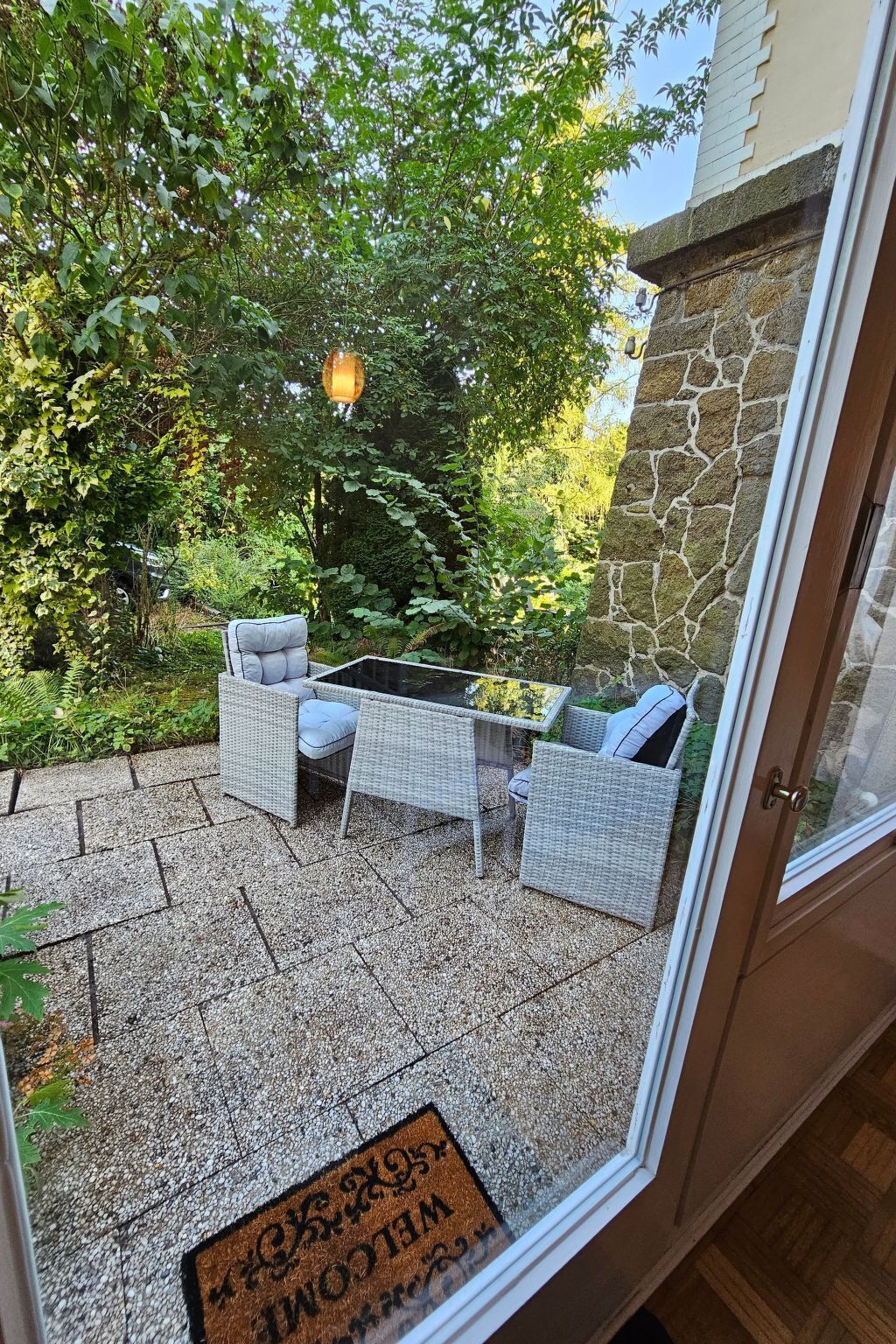Une terrasse avec des meubles en osier, une table en verre et un mur en pierre.