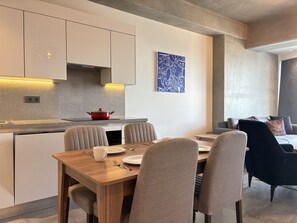 Una cocina moderna con armarios blancos, una olla roja y un comedor con mesa y sillas de madera.